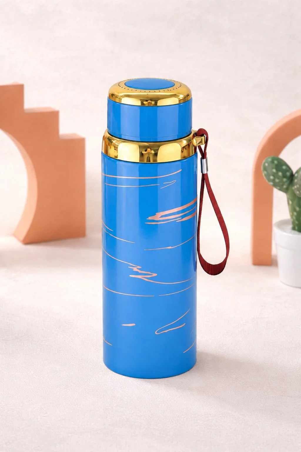 An insulated stainless steel water bottle with gold accents and a wrist strap, designed for hot and cold beverages, displayed in a clean aesthetic studio setting