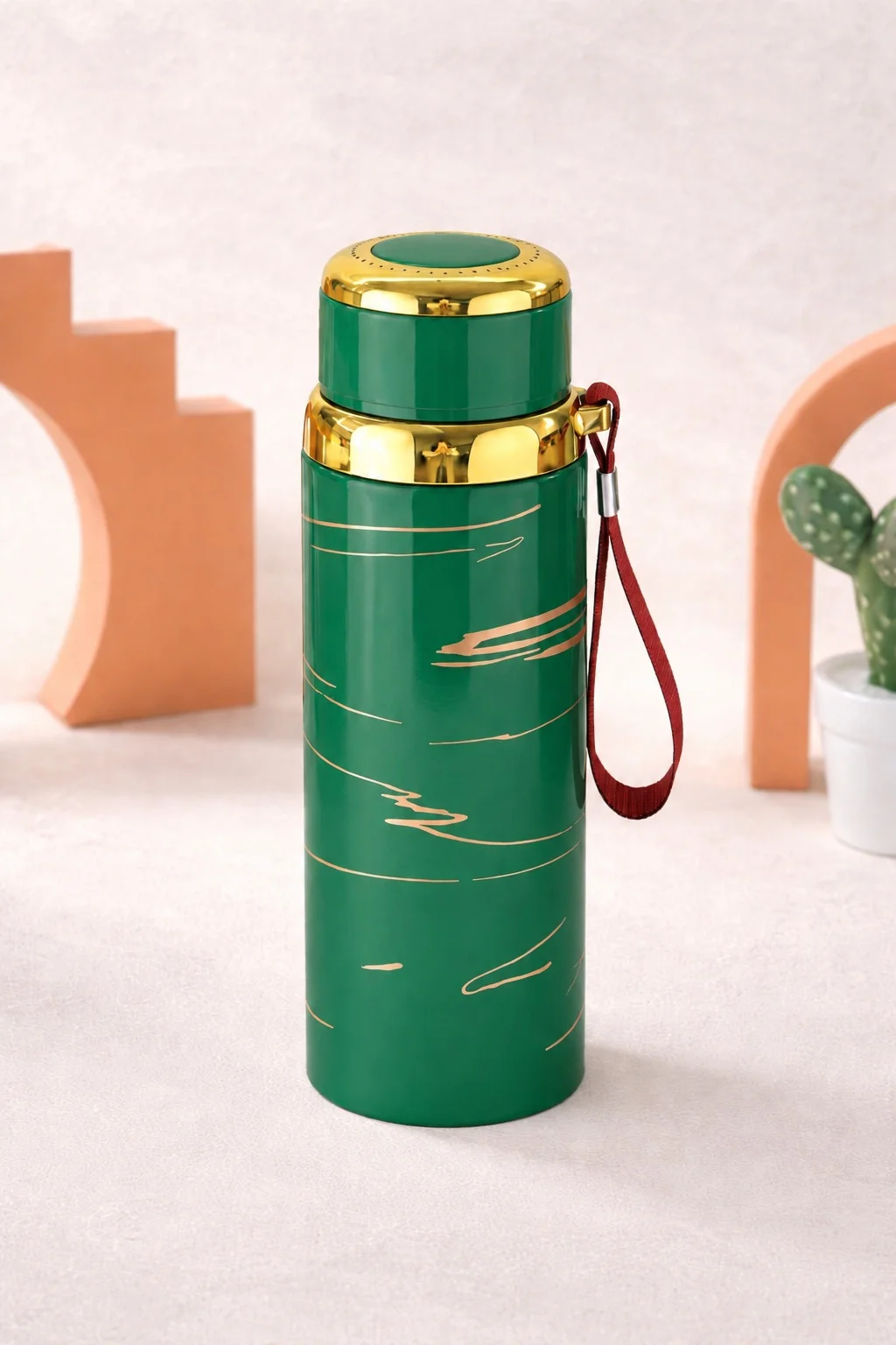 An insulated stainless steel water bottle with gold accents and a wrist strap, designed for hot and cold beverages, displayed in a clean aesthetic studio setting