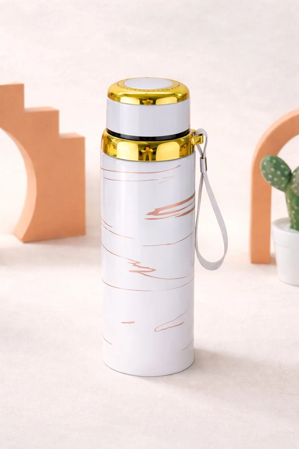 An insulated stainless steel water bottle with gold accents and a wrist strap, designed for hot and cold beverages, displayed in a clean aesthetic studio setting