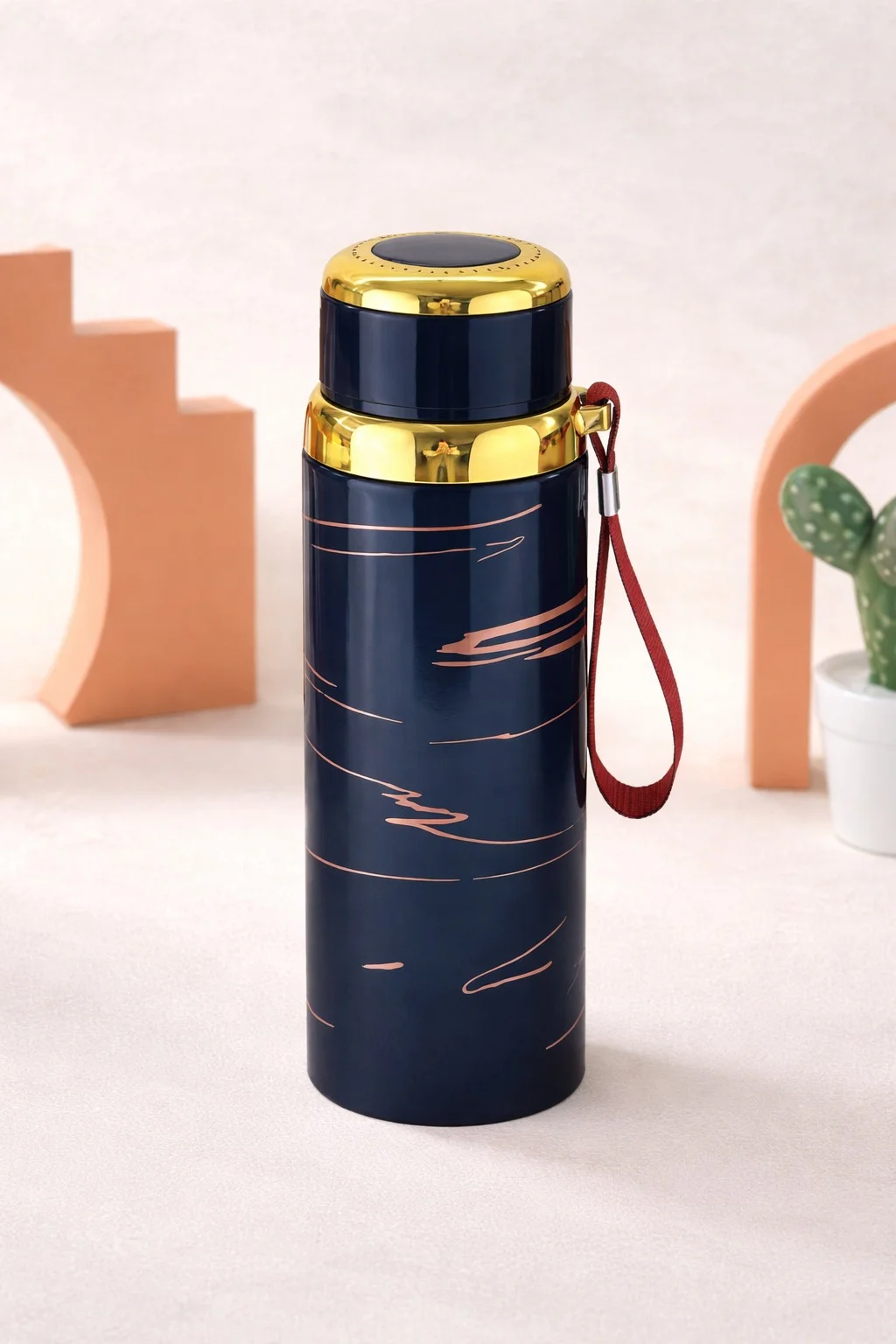 An insulated stainless steel water bottle with gold accents and a wrist strap, designed for hot and cold beverages, displayed in a clean aesthetic studio setting